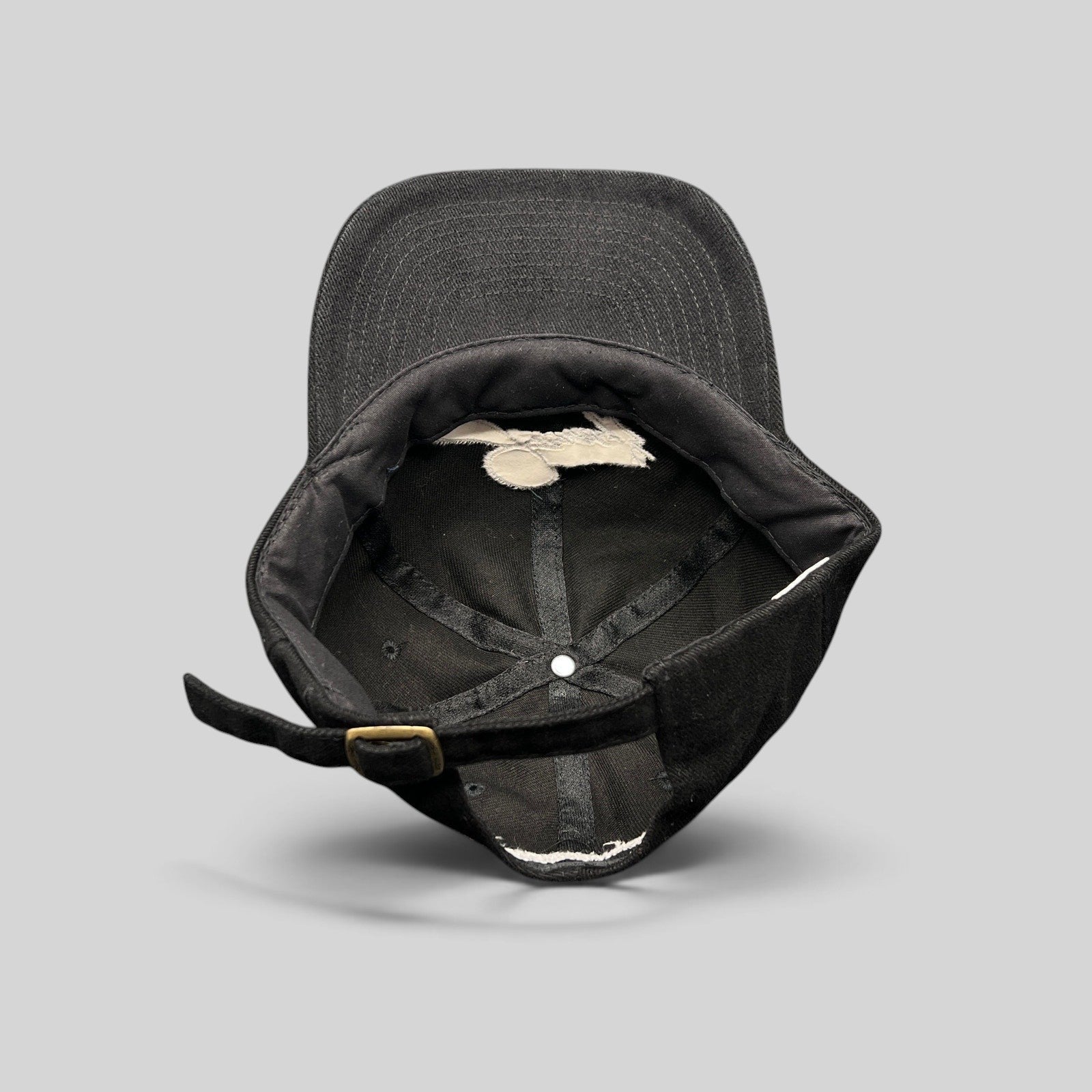 Raree Finds vintage black cotton strapback hat showing the interior unstructured crown and brass-tone buckle closure.