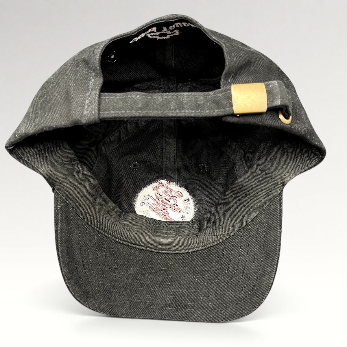 Raree Finds black cotton strapback hat with adjustable brass buckle, showing interior construction and branding.