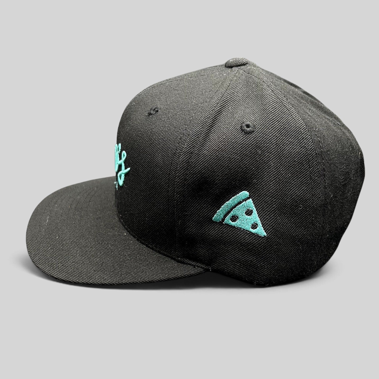 Raree Finds black snapback hat with teal Esco’s Pizza script embroidery and a pizza slice icon on the side panel.