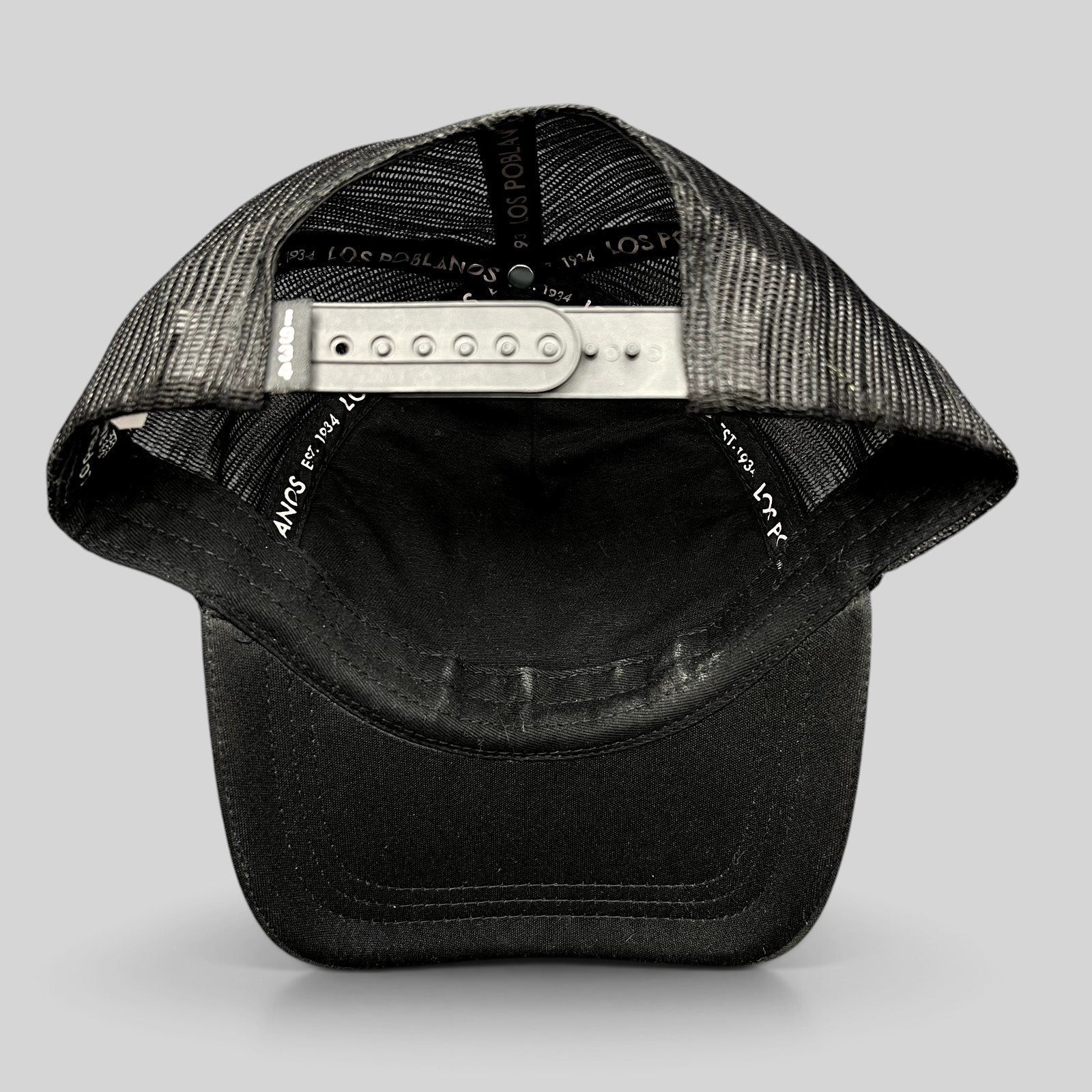 Raree Finds black trucker hat with mesh back, curved brim, and adjustable snapback closure showing interior branding.