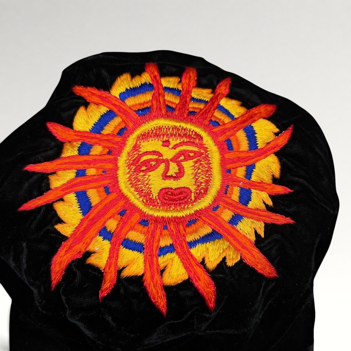 Raree Finds vintage black velvet cap featuring a vibrant embroidered southwestern sun face in red, yellow, and blue.