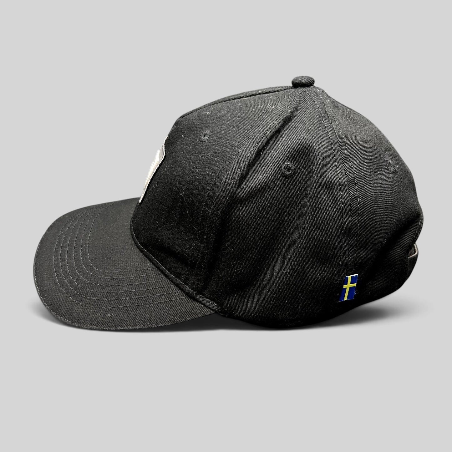 Raree Finds black organic cotton Volvo Iron Mark baseball cap with a small Swedish flag side tag, side profile view.