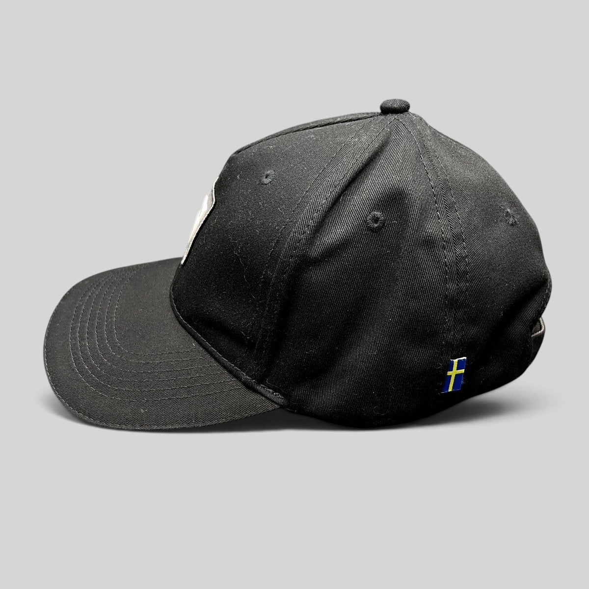 Raree Finds black organic cotton Volvo Iron Mark baseball cap with a small Swedish flag side tag, side profile view.
