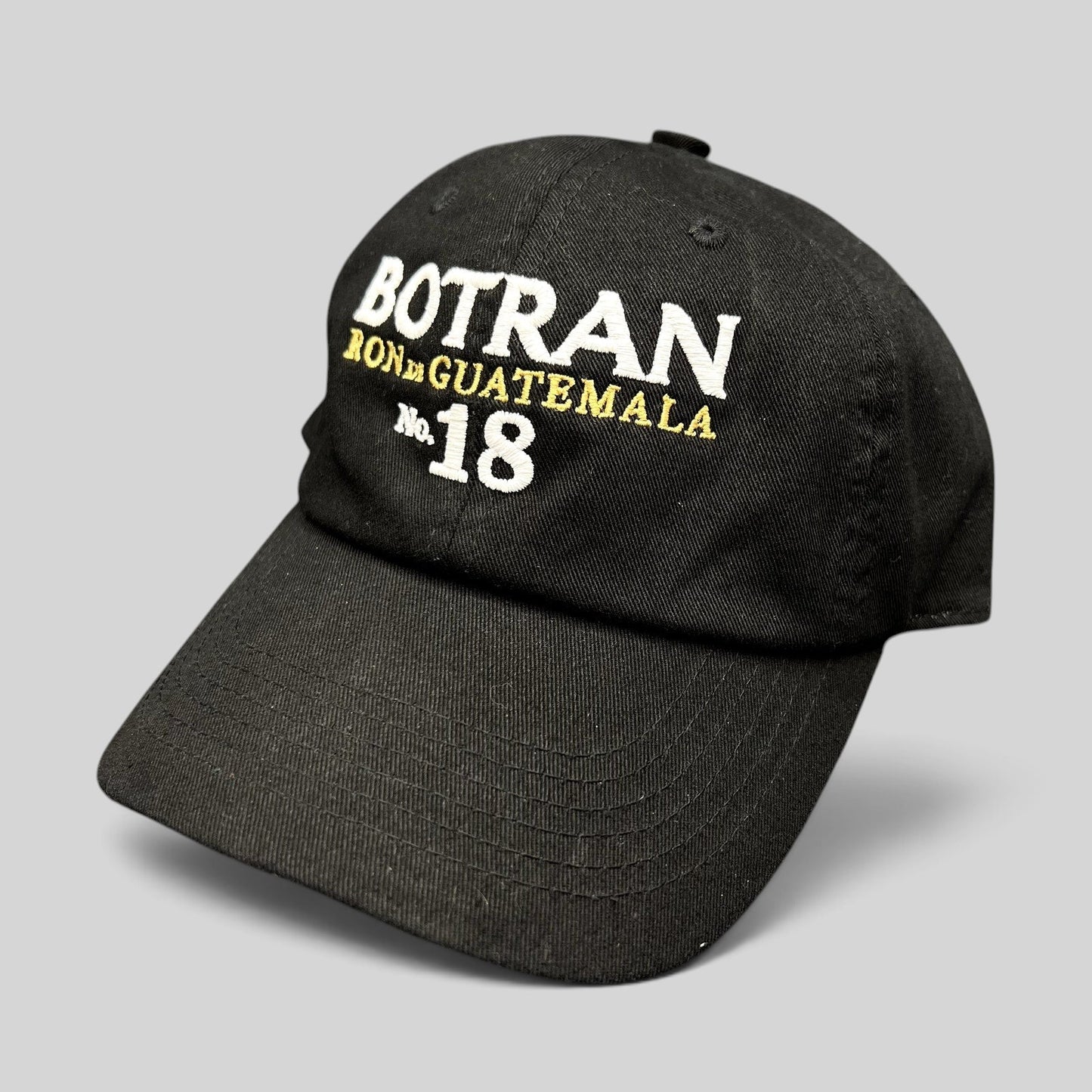 Raree Finds black cotton strapback hat featuring white and gold Botran Ron De Guatemala No 18 embroidery