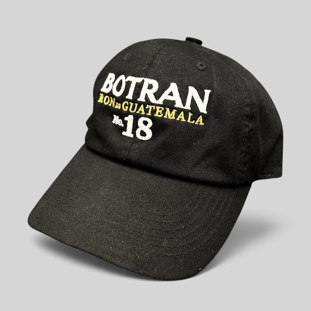 Raree Finds black cotton strapback hat featuring white and gold Botran Ron De Guatemala No 18 embroidery