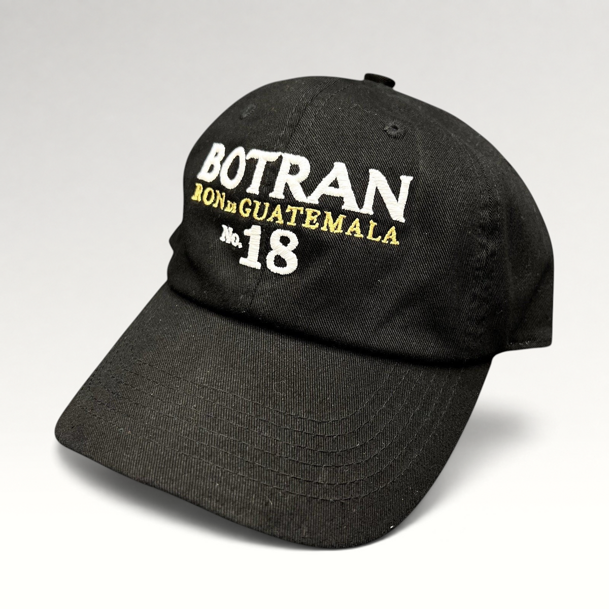 Raree Finds black cotton strapback hat featuring white and gold Botran Ron De Guatemala No 18 embroidery