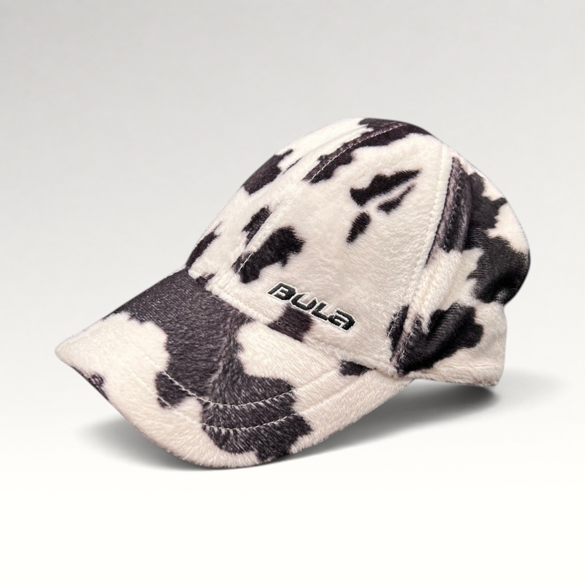 Raree Finds BULA black and white cow print plush fleece baseball cap with curved brim and side logo embroidery.