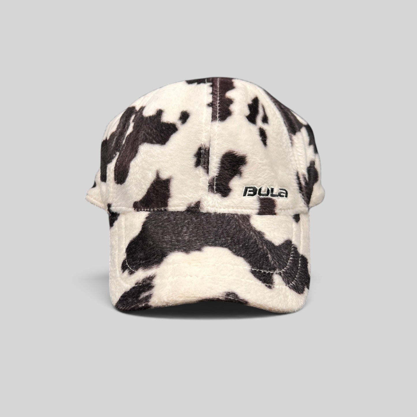 Raree Finds BULA plush fleece baseball cap in a black and white cow print with an unstructured crown and curved brim.
