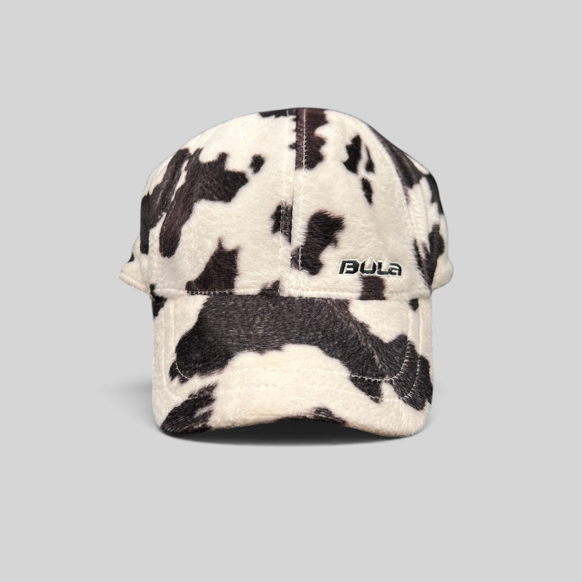 Raree Finds BULA plush fleece baseball cap in a black and white cow print with an unstructured crown and curved brim.
