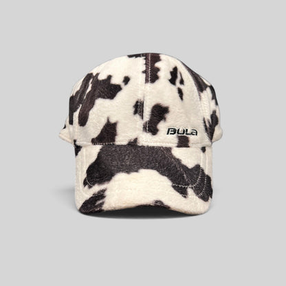 Raree Finds BULA plush fleece baseball cap in a black and white cow print with an unstructured crown and curved brim.