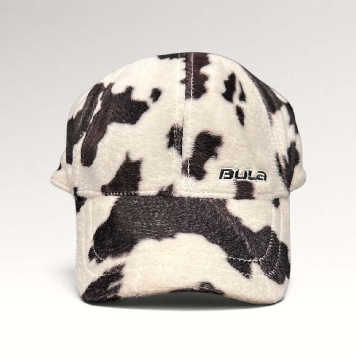 Raree Finds BULA plush fleece baseball cap in a black and white cow print with an unstructured crown and curved brim.