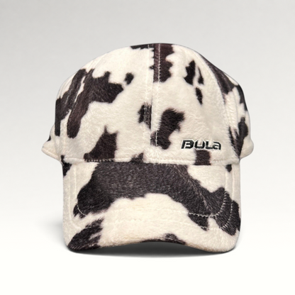 Raree Finds BULA plush fleece baseball cap in a black and white cow print with an unstructured crown and curved brim.