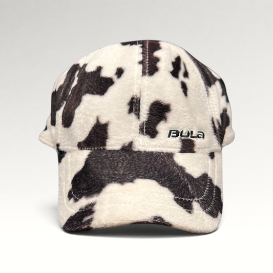 Raree Finds BULA plush fleece baseball cap in a black and white cow print with an unstructured crown and curved brim.