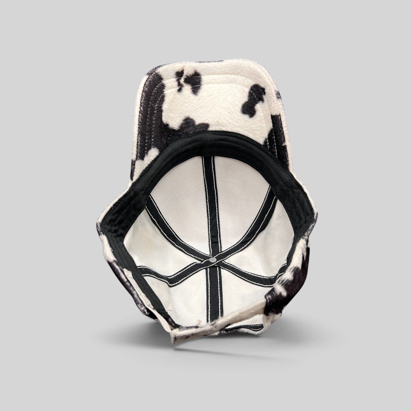 Raree Finds BULA black and white cow print plush fleece cap showing the interior lining and adjustable back strap.