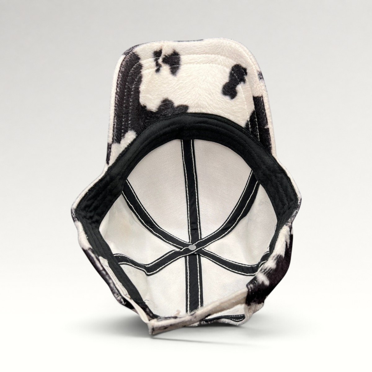 Raree Finds BULA black and white cow print plush fleece cap showing the interior lining and adjustable back strap.