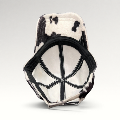 Raree Finds BULA black and white cow print plush fleece cap showing the interior lining and adjustable back strap.