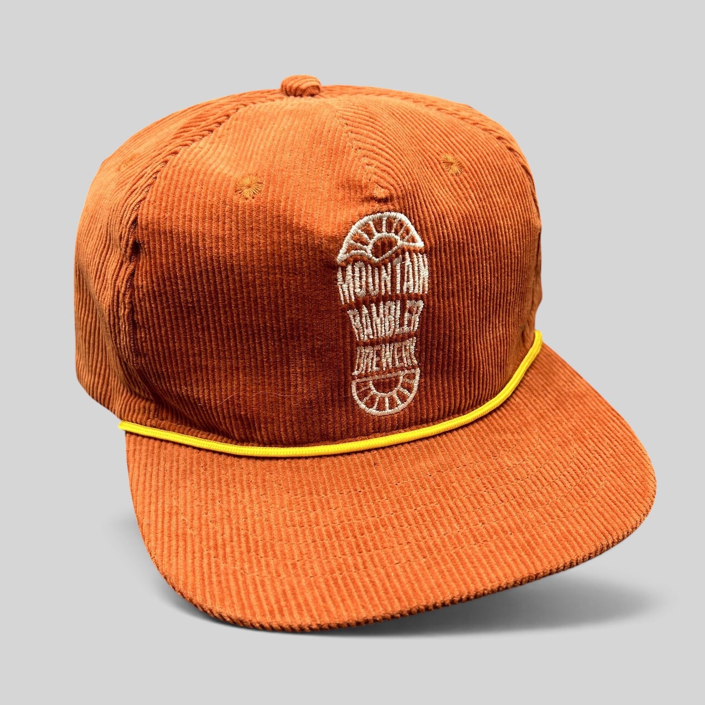 Raree Finds burnt orange corduroy snapback hat with yellow rope trim and Mountain Rambler Brewing boot-print logo.