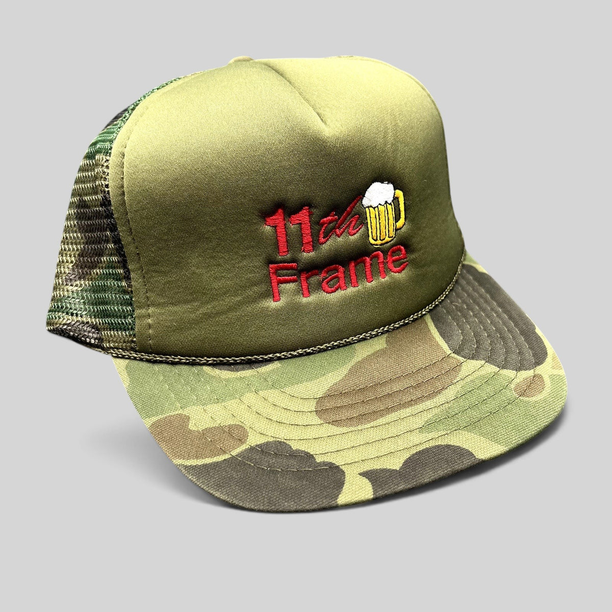 Raree Finds vintage 11th Frame trucker hat with olive foam front, woodland camo brim, and embroidered beer mug logo.