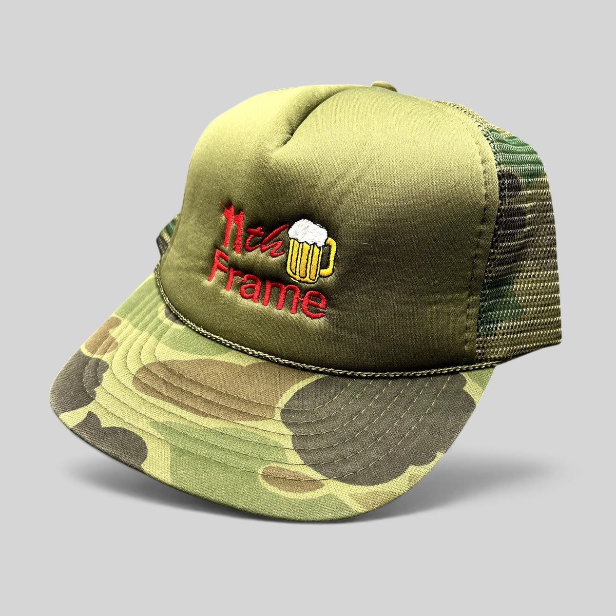 Raree Finds vintage 11th Frame trucker hat with olive foam front, woodland camo brim, mesh back, and beer logo.