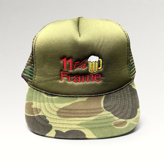 Raree Finds vintage 11th Frame trucker hat with olive foam front, woodland camo brim, and embroidered beer mug logo.