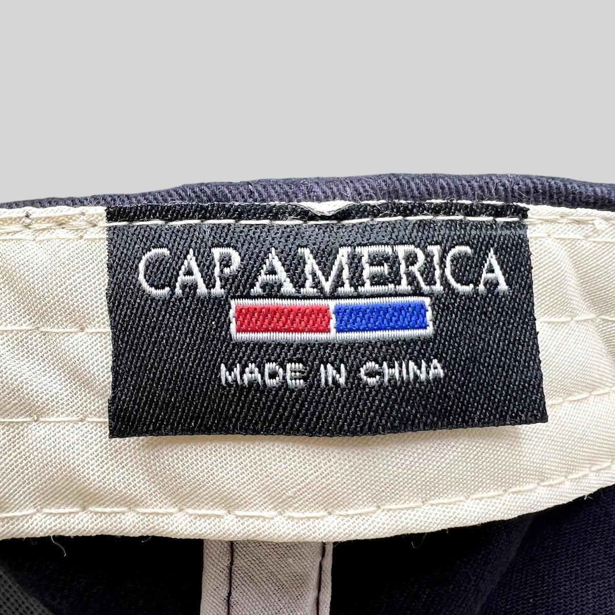 Raree Finds Cap America interior woven brand label featuring white text on a black background inside a navy hat