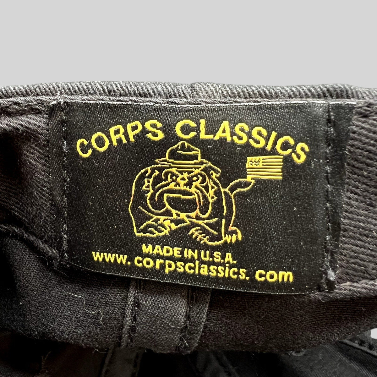 Raree Finds Corps Classics black fabric hat label with yellow embroidered bulldog mascot and American flag logo