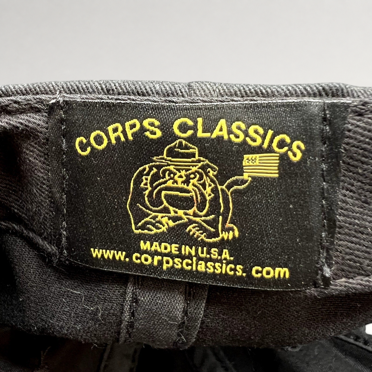 Raree Finds Corps Classics black fabric hat label with yellow embroidered bulldog mascot and American flag logo