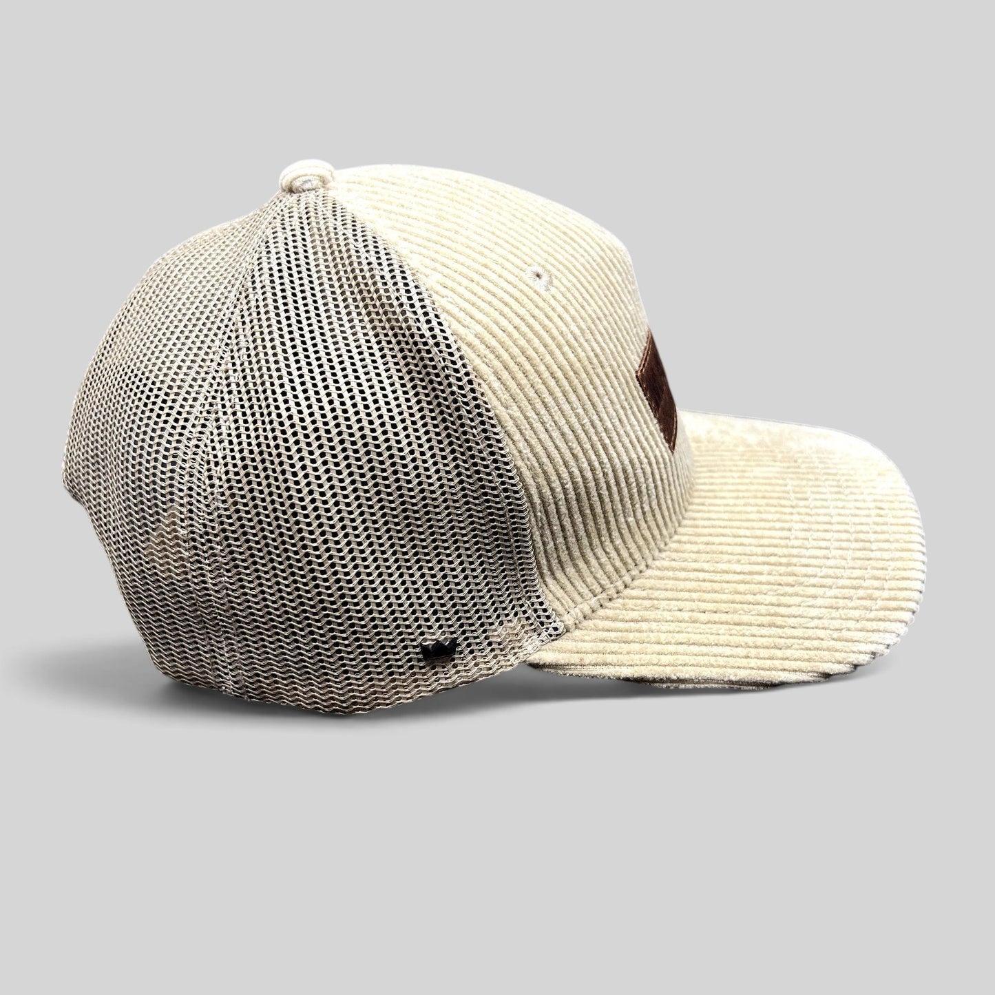 Raree Finds cream corduroy trucker hat with mesh back, curved brim, and leather patch, side view.