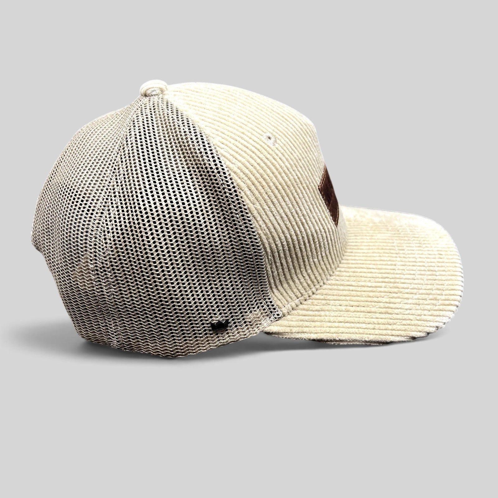 Raree Finds cream corduroy trucker hat with mesh back, curved brim, and leather patch, side view.