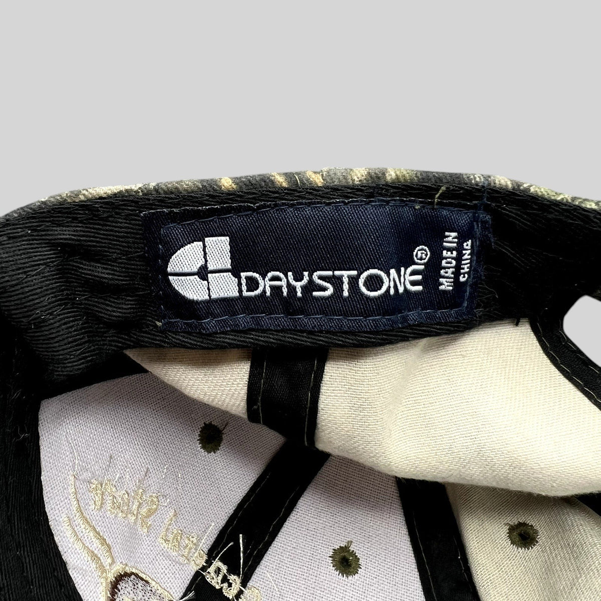 Raree Finds Daystone brand label inside a woodland camouflage strapback hat with embroidered interior details