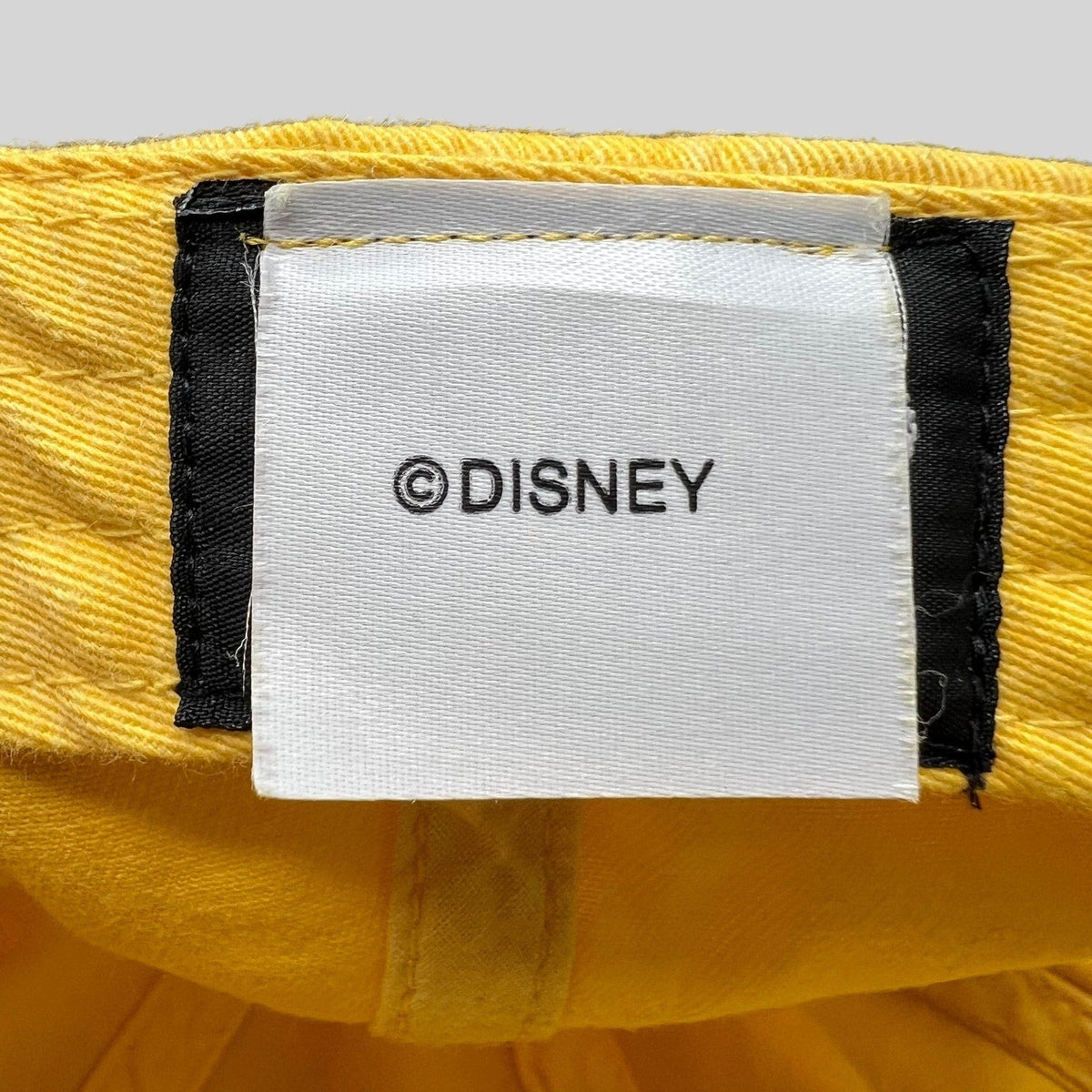 Raree Finds Disney VoluntEARS hat interior tag with white fabric and black Disney branding on a yellow cotton crown