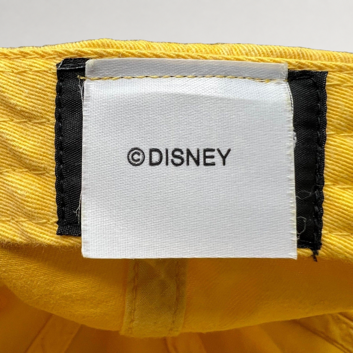 Raree Finds Disney VoluntEARS hat interior tag with white fabric and black Disney branding on a yellow cotton crown