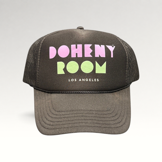 Raree Finds black mesh trucker hat with Doheny Room pastel logo on a structured foam front panel and curved brim.
