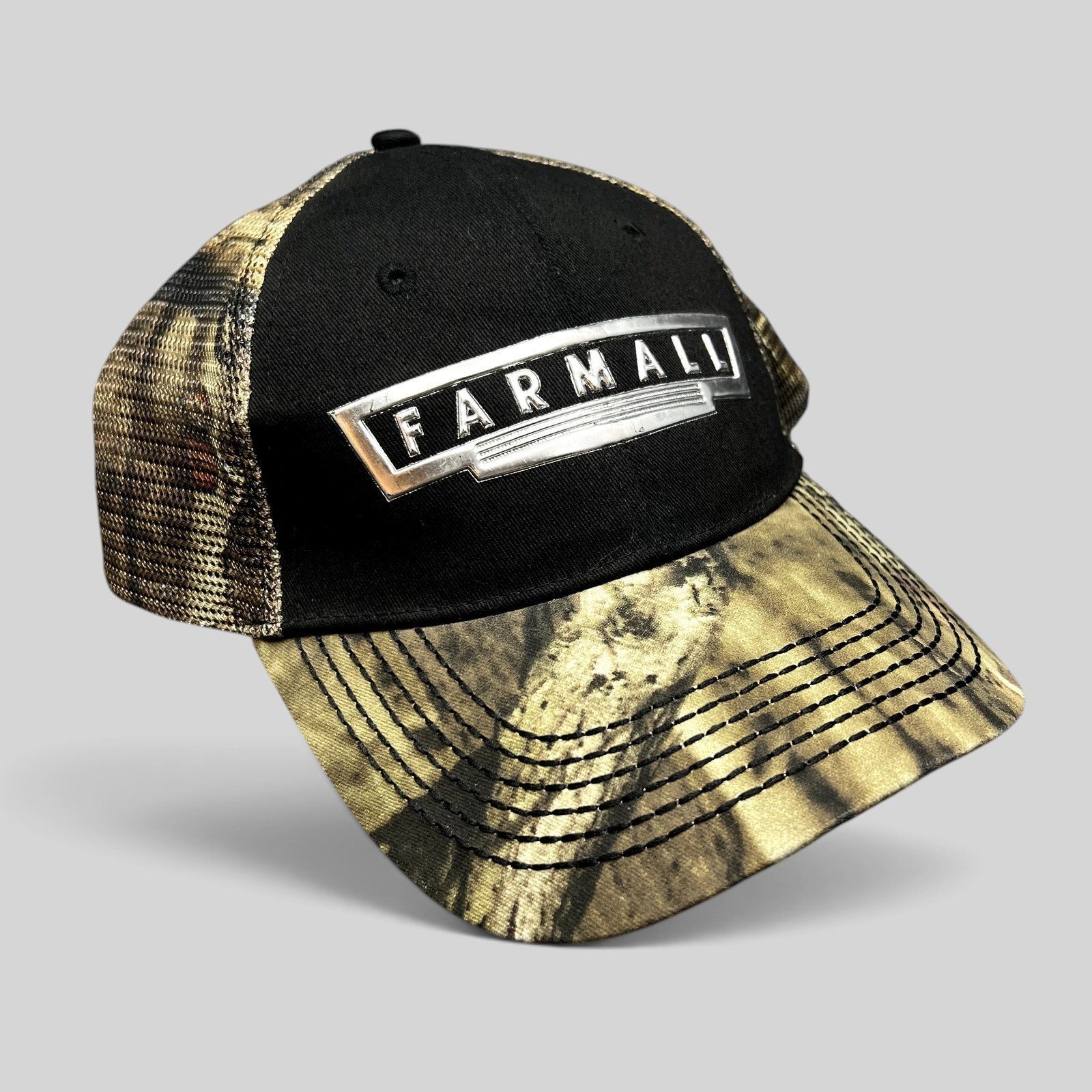 Raree Finds Farmall trucker hat with black cotton crown, camouflage mesh back, and metallic logo patch on curved brim