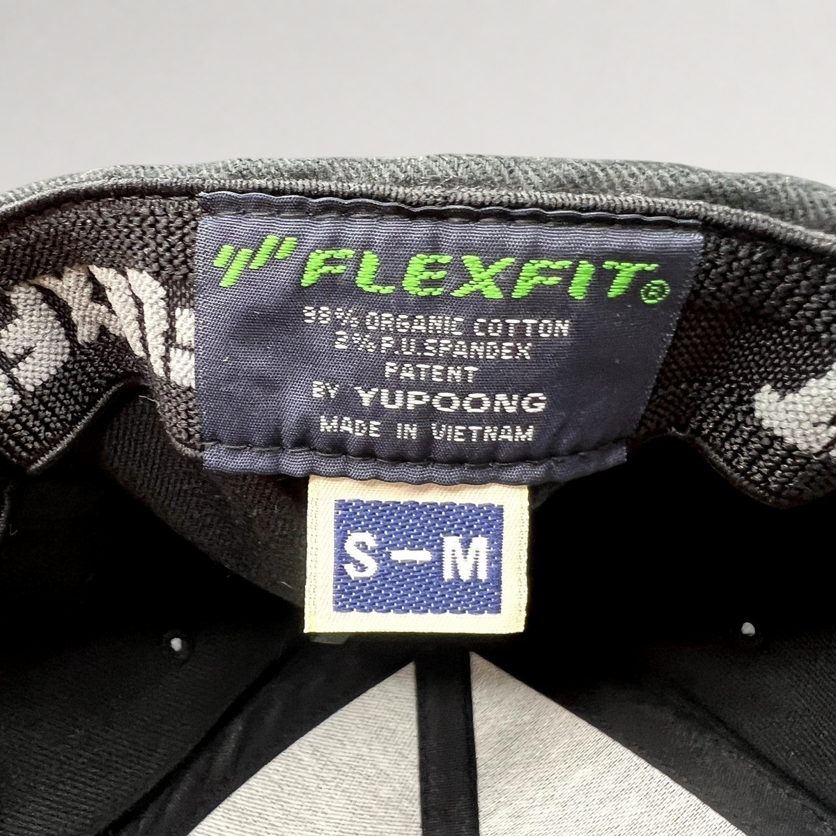 Raree Finds black Yupoong Flexfit hat interior label showing size S-M, organic cotton blend, and Vietnam origin.