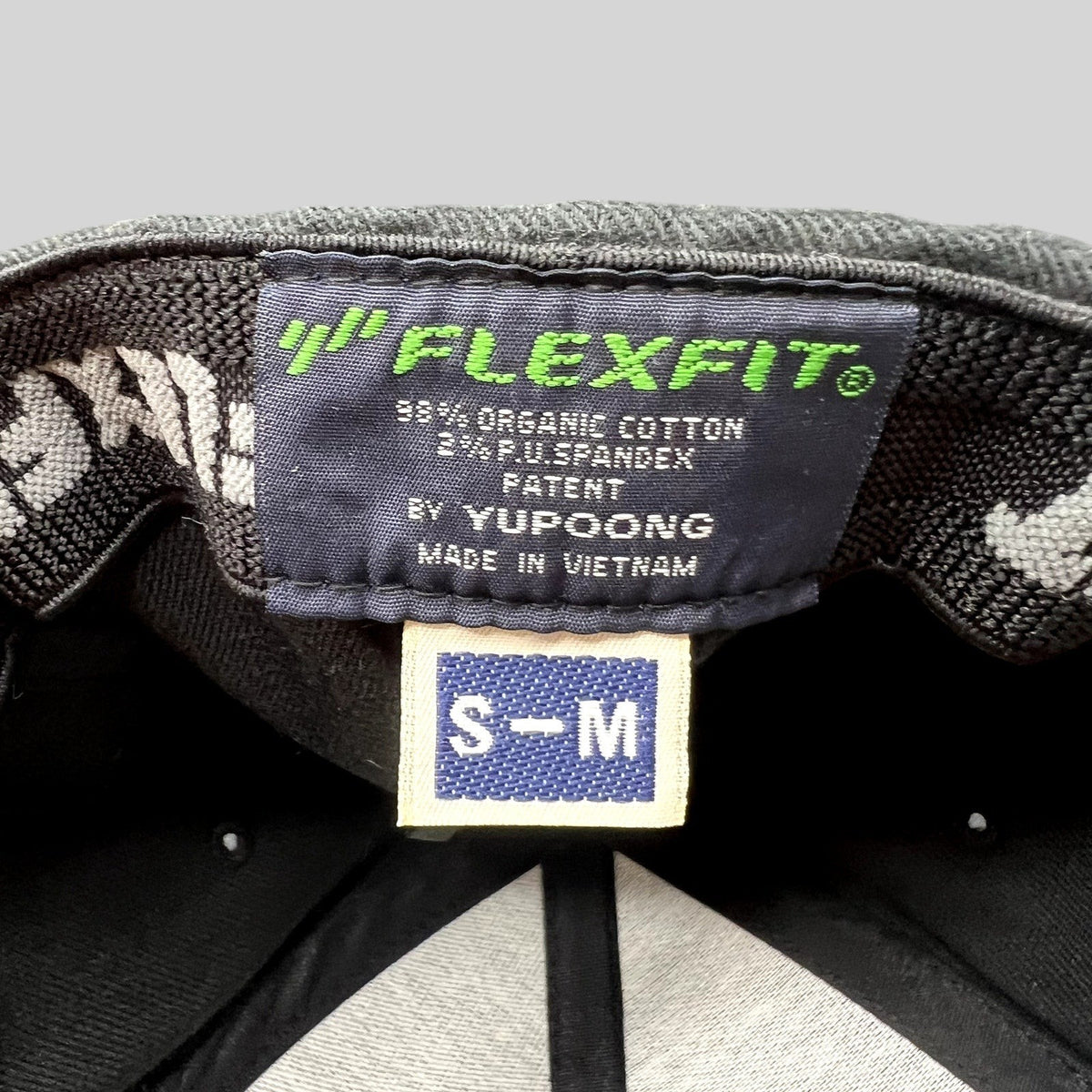 Raree Finds black Yupoong Flexfit hat interior label showing size S-M and material composition