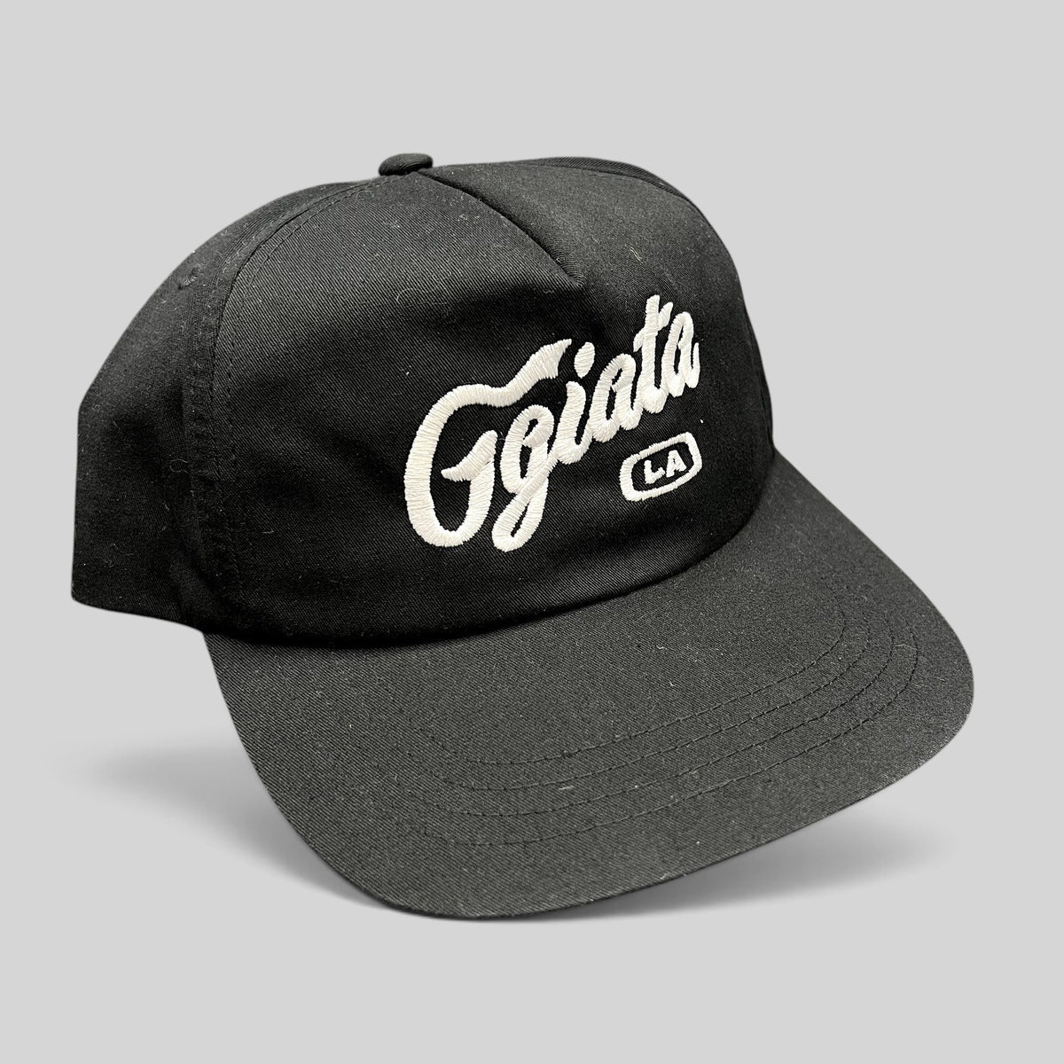Raree Finds black Ggiata LA snapback hat with white embroidered script logo and flat brim on a structured crown.