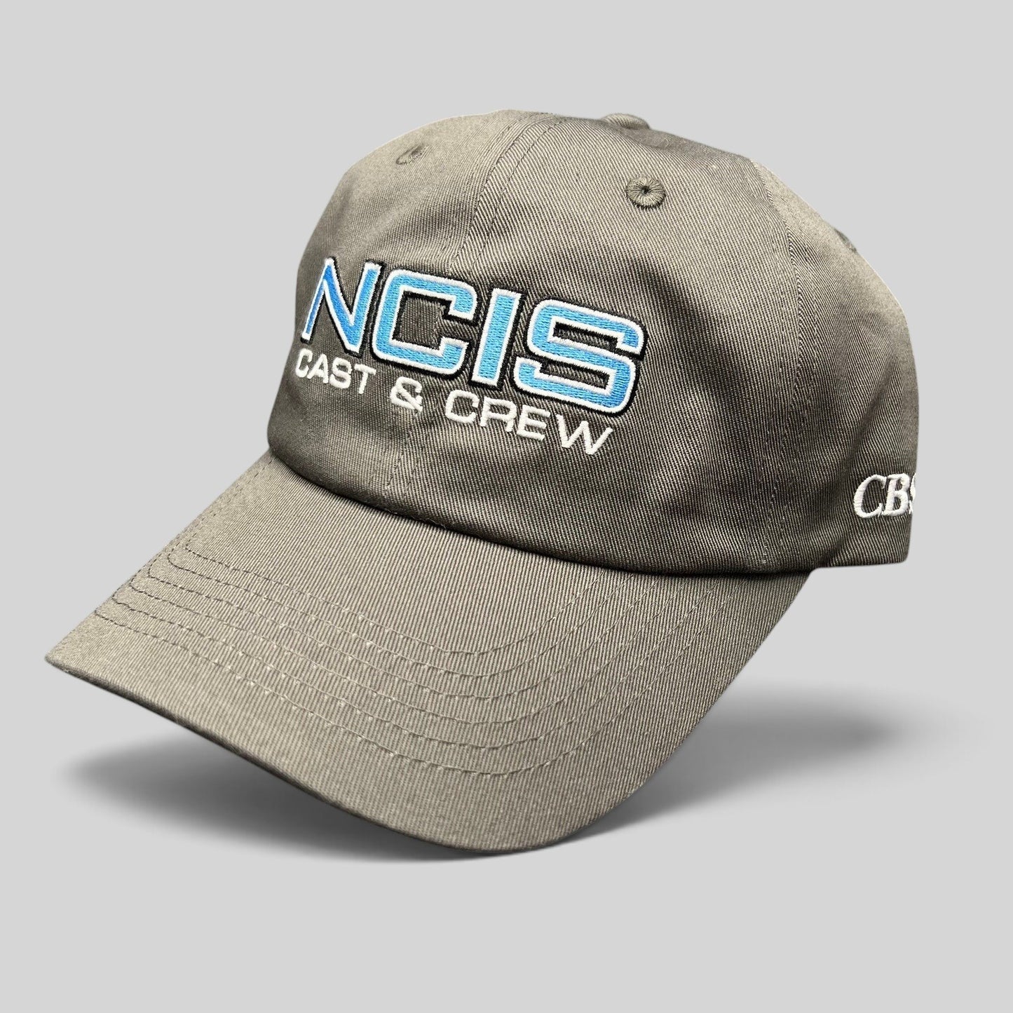 Raree Finds gray NCIS Cast & Crew strapback hat with blue and white embroidered logo and curved bill.