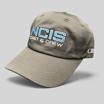 Raree Finds gray NCIS Cast & Crew strapback hat with blue and white embroidered logo and curved bill.