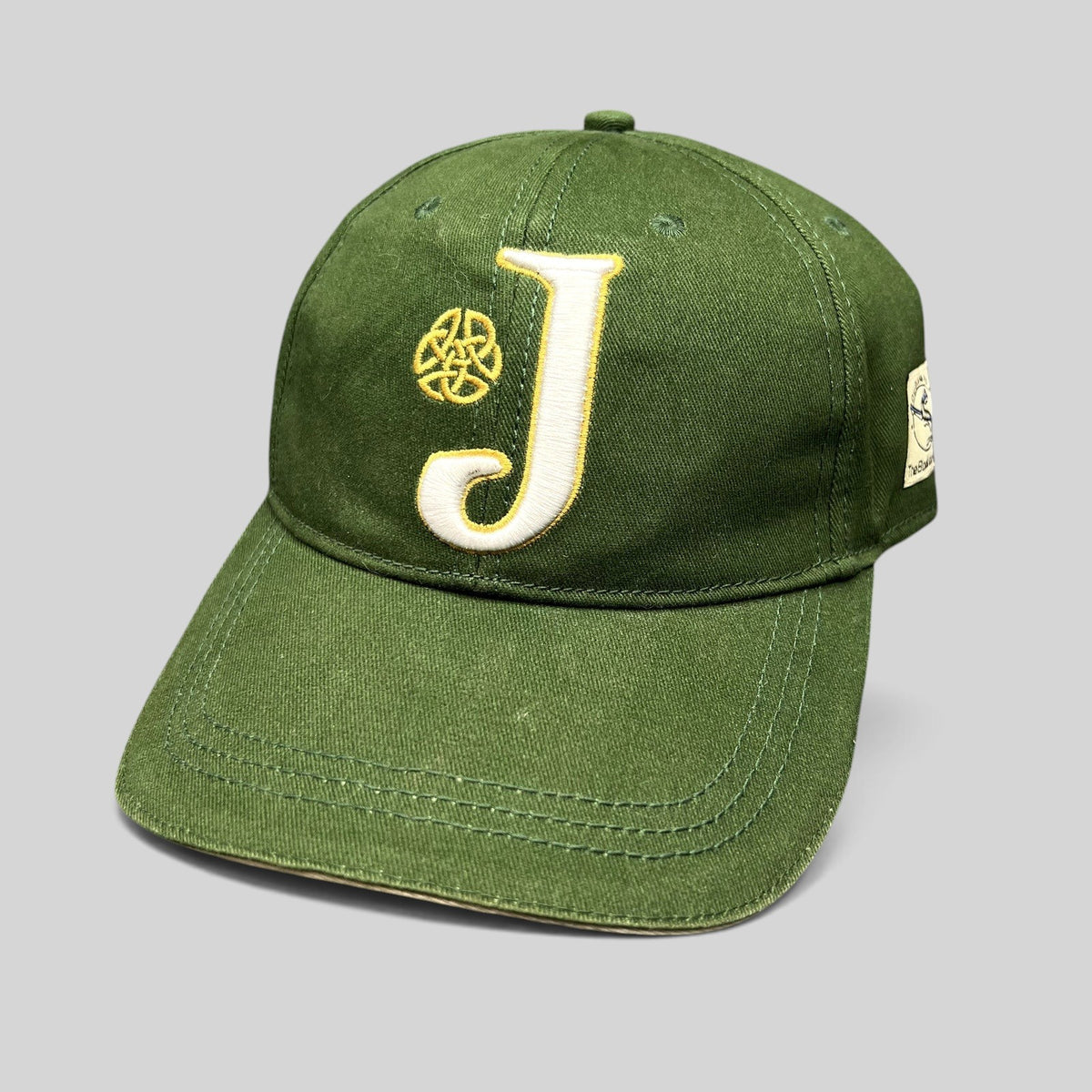Raree Finds dark green strapback hat featuring an embroidered white J logo and gold Celtic knot detail.