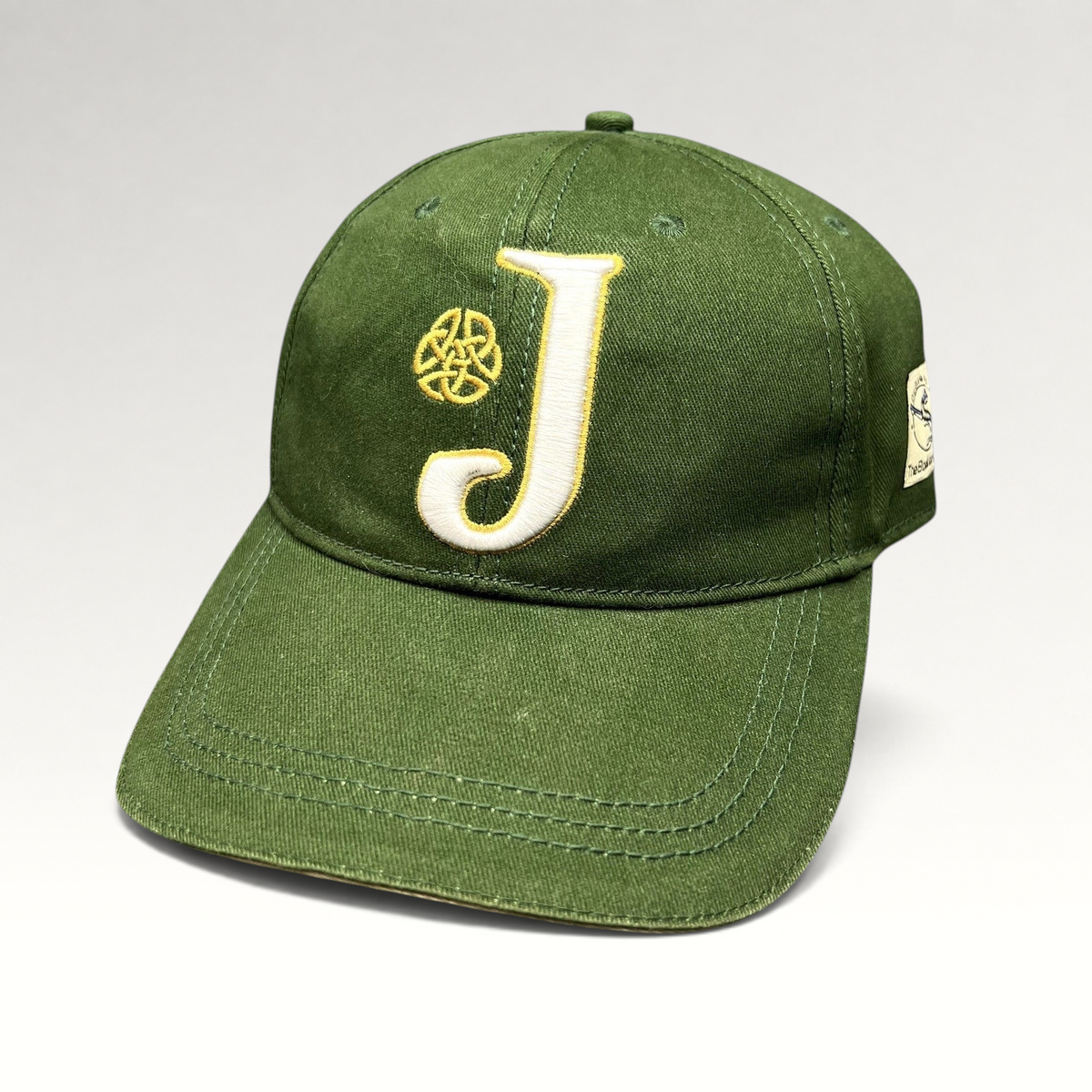 Raree Finds dark green strapback hat featuring an embroidered white J logo and gold Celtic knot detail.