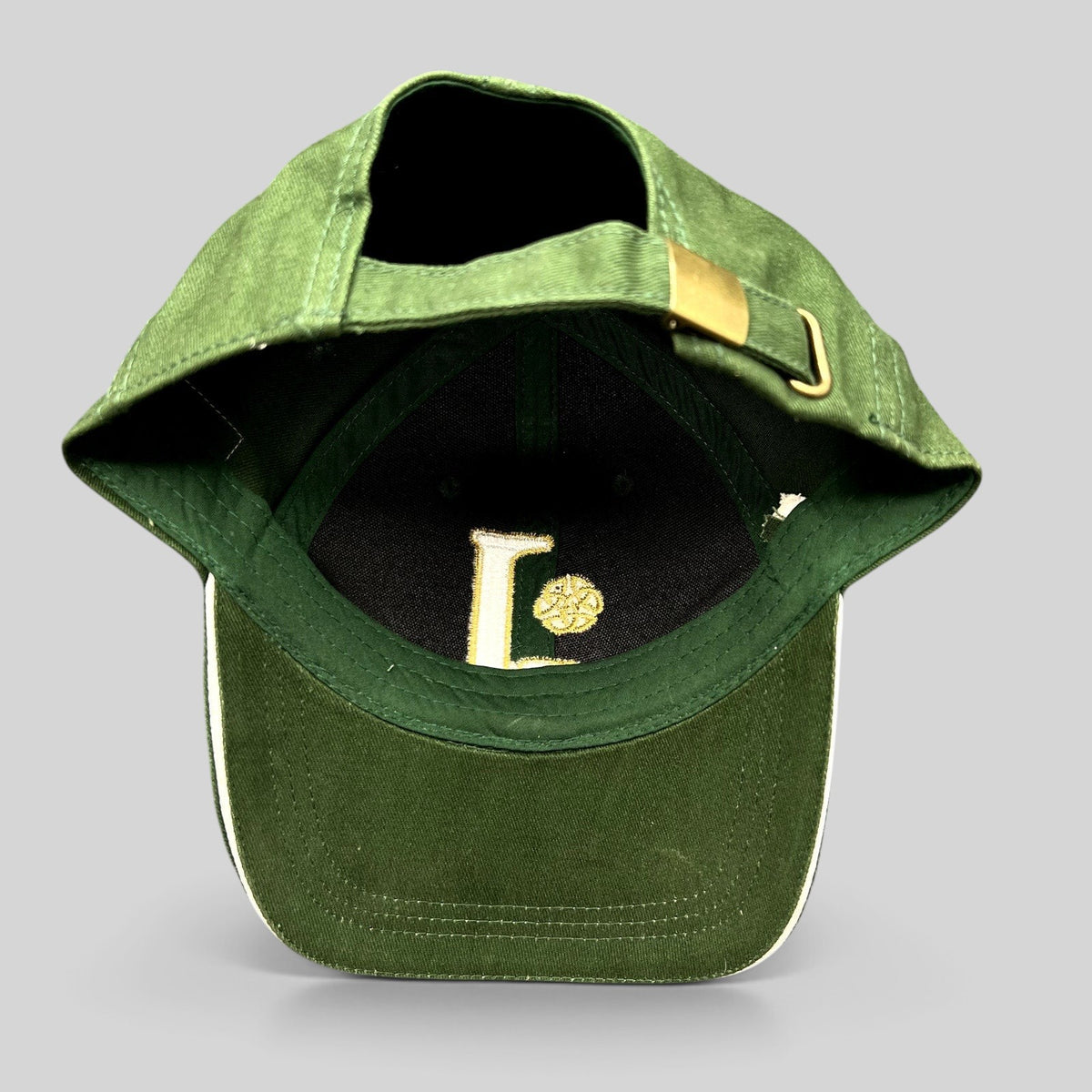 Raree Finds dark green strapback hat with gold Celtic knot embroidery and brass buckle adjuster, interior view.