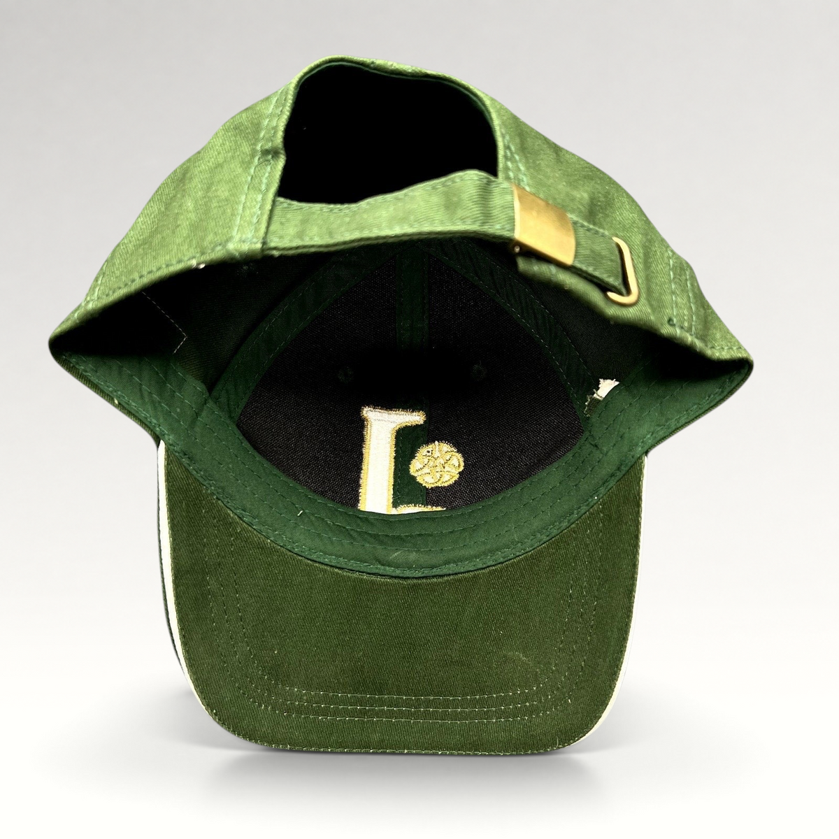 Raree Finds dark green strapback hat with gold Celtic knot embroidery and brass buckle adjuster, interior view.