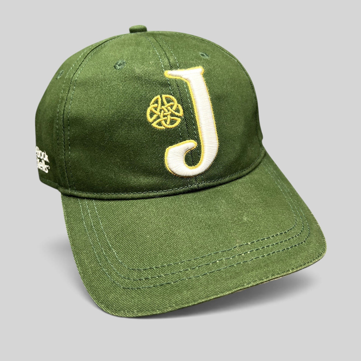 Raree Finds dark green strapback hat with an embroidered white J logo and gold Celtic knot, inspired by Book of Kells.