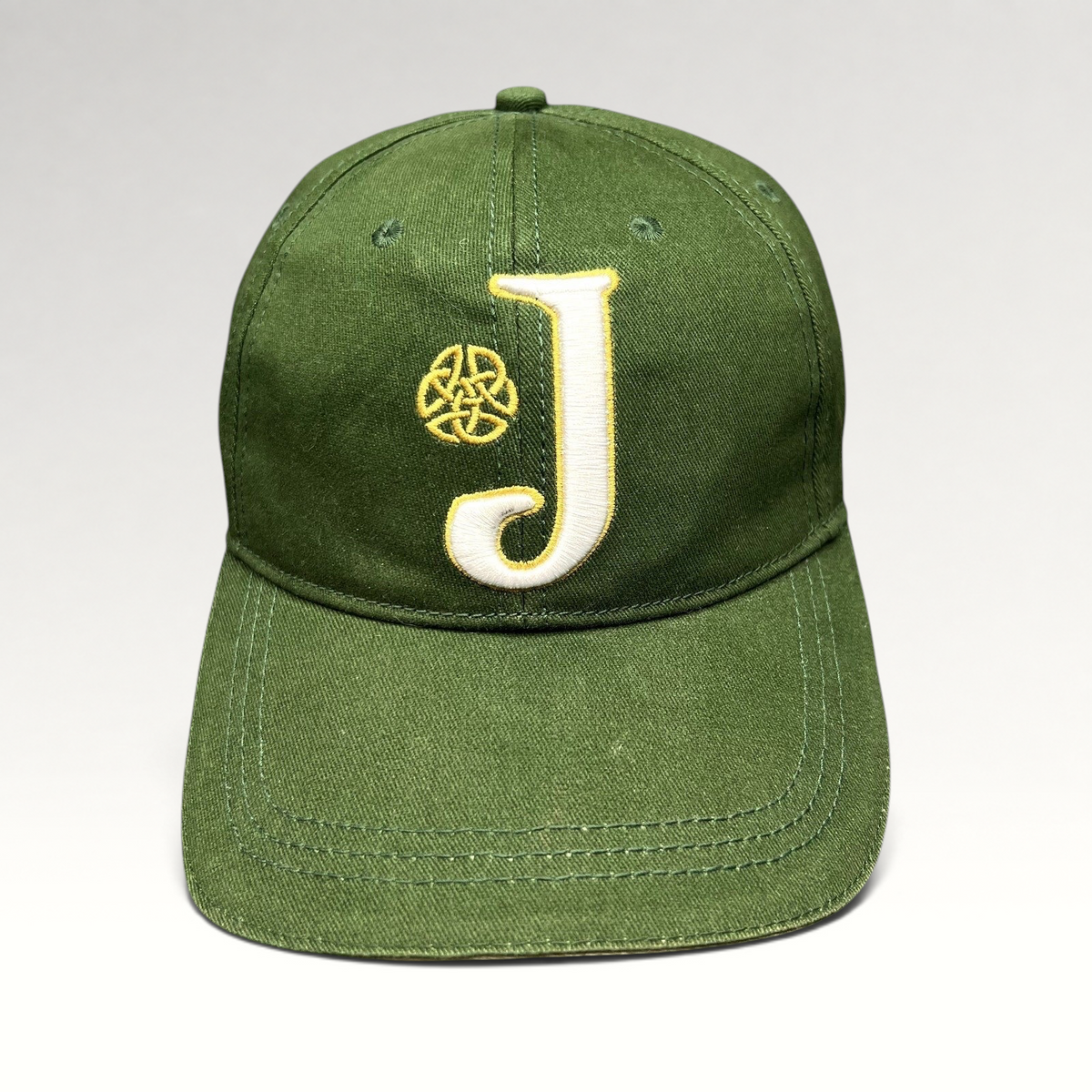 Raree Finds dark green strapback hat with an embroidered white J logo and gold Celtic knot symbol on the front.