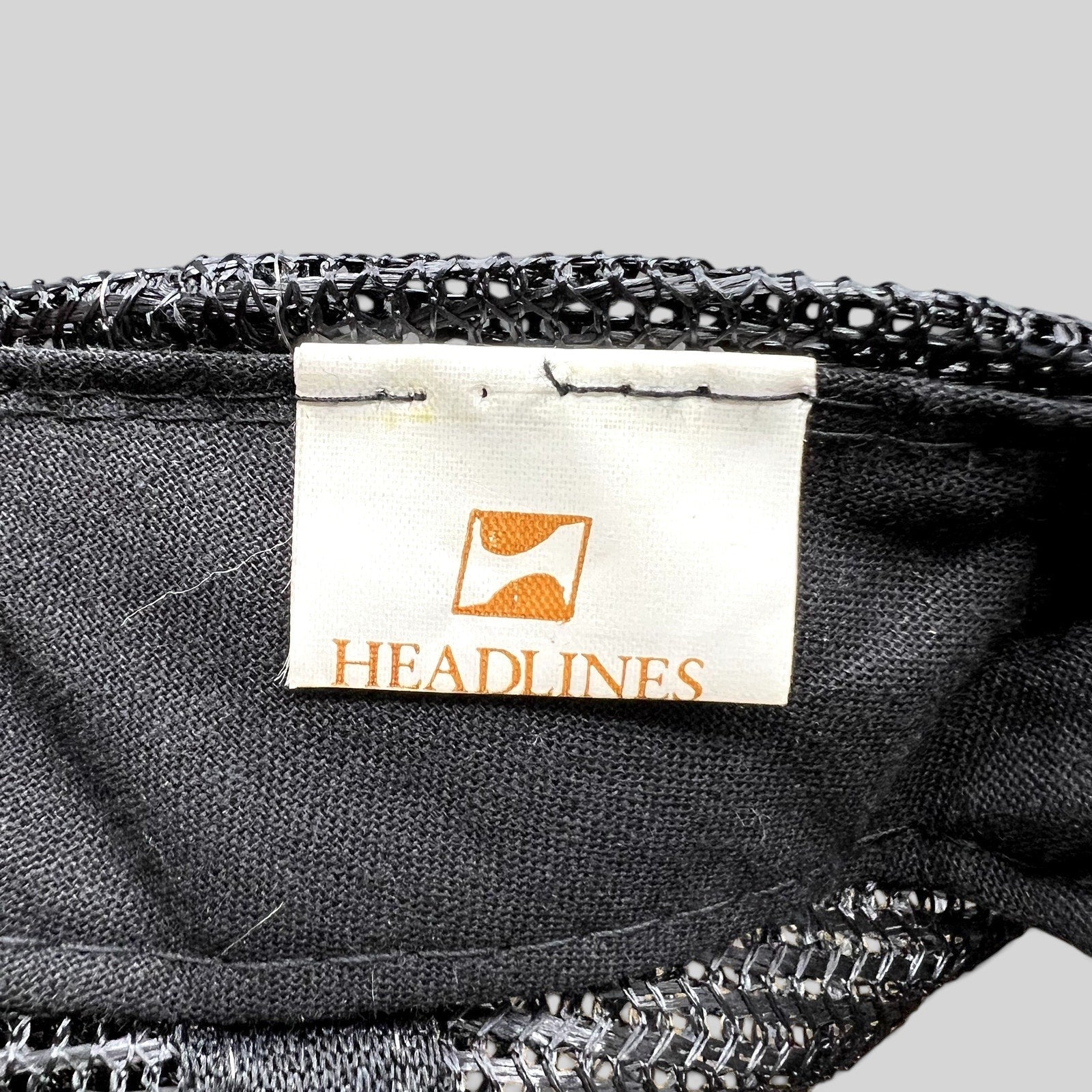 Raree Finds vintage Headlines brand tag inside a black mesh trucker hat with white fabric and orange logo detail