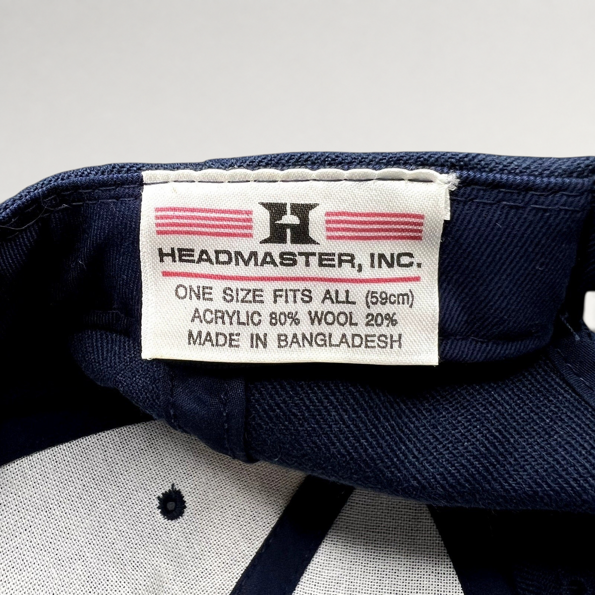 Raree Finds Headmaster hat interior tag showing brand logo, material composition, and origin on navy blue fabric