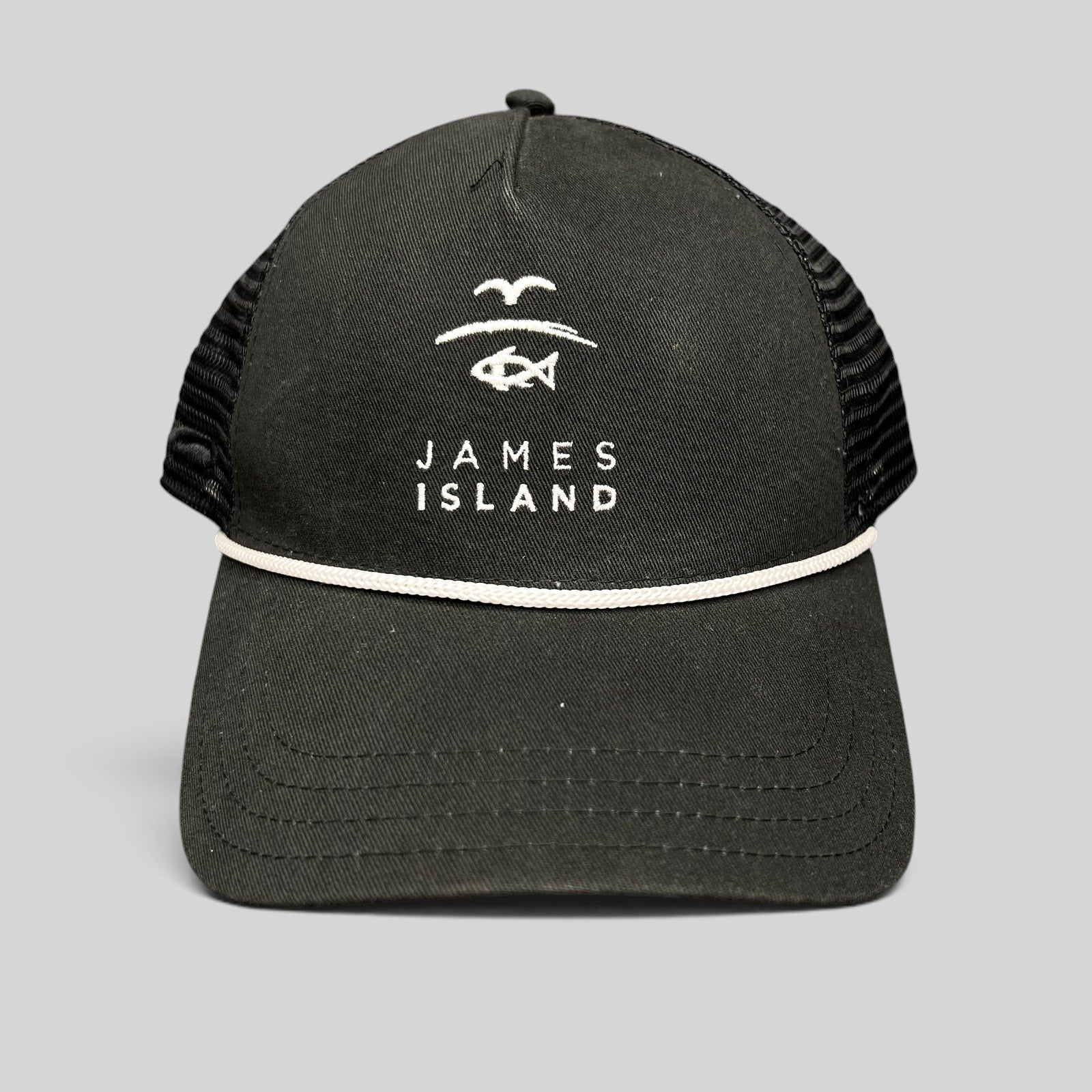 Raree Finds black trucker hat with white James Island coastal logo embroidery, mesh back, and rope detail on brim.