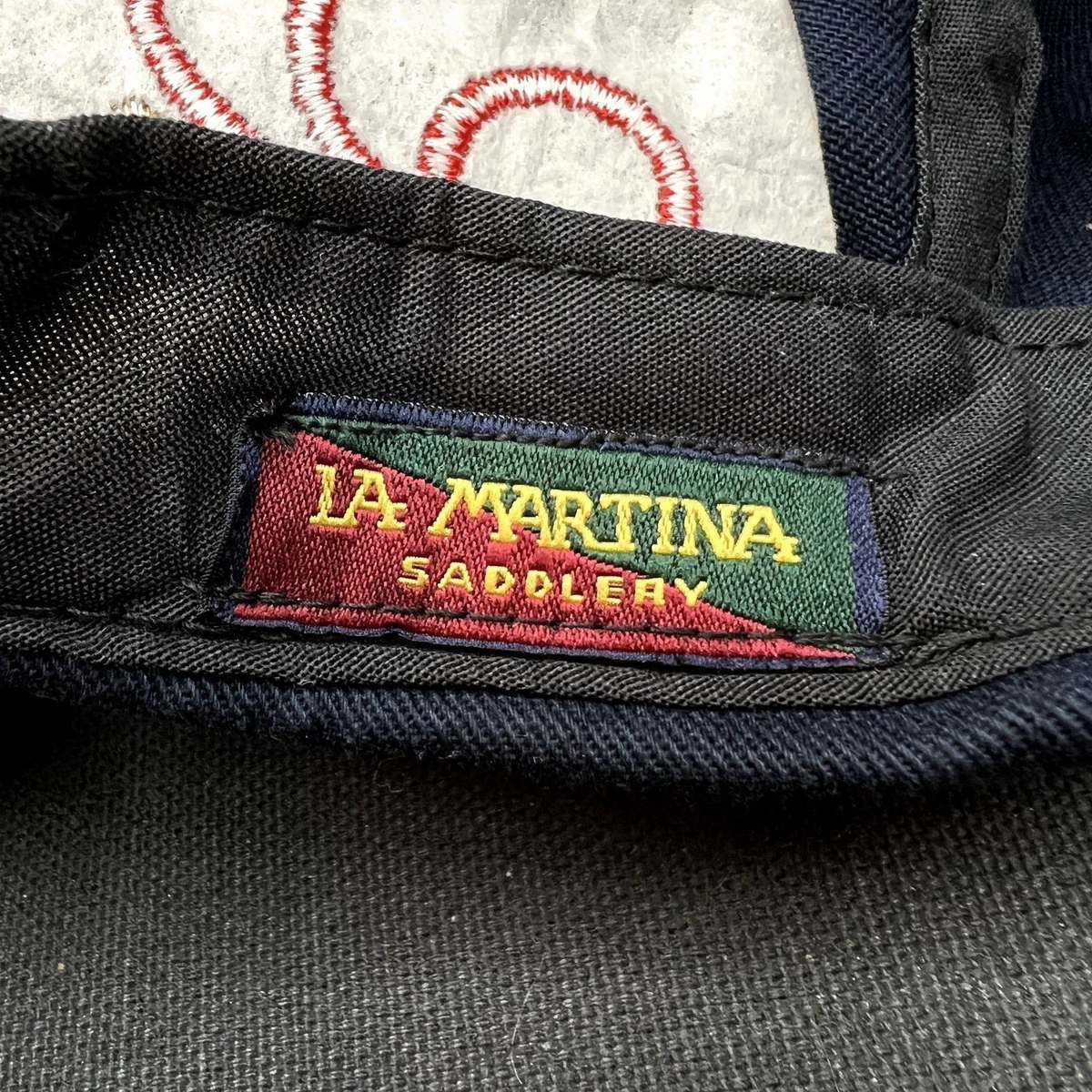 Raree Finds vintage La Martina Saddlery interior woven brand label in red, green, and gold on navy blue cotton fabric.