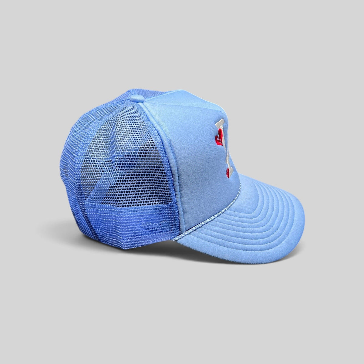 Raree Finds light-blue Y2K trucker hat with white LA logo and red broken-heart embroidery on a foam front mesh cap.